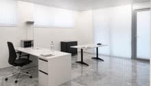 A minimalist office room with white walls and floors, featuring two desks with chairs, a small table, a cabinet, a lamp, and two bottles on the desks.