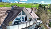 Modern house, brown roof, glass walls, balcony, outdoor dining area, green field view