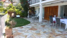 stone floored patio with dining table, chairs, 2 lounge chairs, balcony, shrubs and trees