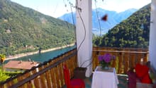 Balcony with wooden railings, red chair, white table with flowers, red pillows, view of mountains and lake