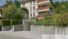 Multistory building, white walls, brown roof, wooden balconies, garage, concrete stairs, trees and shrubs