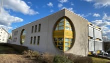 Modern building with a white brick facade, large yellow arched windows, and a circular window on the front.