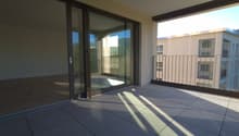 Balcony with sliding glass doors, tiled floor, metal railing, view of another building and trees