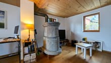 Cozy living room with wooden ceiling, stone fireplace, desk with computer, bookshelves, and a small table with chairs.