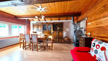 Rustic wooden interior with exposed beams, large wooden dining table and chairs, antique wooden cabinets, wood-burning stove, and decorative star-shaped light fixture