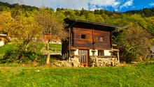 small wooden house, situated on a hill, surrounded by trees and grass, view of mountains