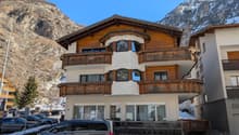 Three story building, wooden balconies, white walls, gray trim, glass windows, snow-covered mountain in the background