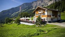 Traditional Swiss chalet with restaurant, balcony with tables, flag, surrounded by grass and mountains