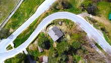 Aerial view of a house surrounded by lush green vegetation, with a winding road passing by the property.