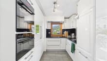 Spacious modern kitchen with white cabinets, black countertops, stainless steel appliances including a dishwasher, and large windows providing a scenic view.
