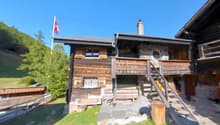 2-story wooden chalet-style house, with a balcony and porch, surrounded by trees and greenery