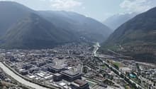 Aerial view of a city with mountains in the background, large buildings, wide river, and trees and plants lining the streets.