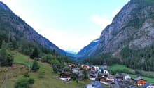 cluster of houses, green trees, rocky mountains, church, grassy fields