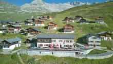 Collection of vacation houses, located on a hillside, surrounded by mountains, with an outdoor dining area.