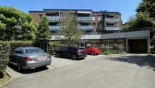 3-story brick apartment building with balconies, surrounded by trees, with a parking lot in the front
