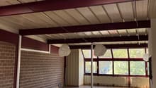 Empty room with brick wall, wooden floor, exposed ceiling beams, two large windows with white curtains, skylight, three hanging lamps