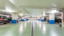 Underground parking lot with multiple cars parked, white and blue pillars, green floor, white ceiling, lights