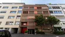 4 story building, red doors, multiple windows, beige and brown exterior, tree in front
