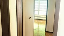 Hallway with hardwood floors, white walls, and a window with blinds. There are two doors leading to other rooms.