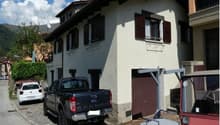 2-story house with white exterior walls, red shutters, and a garage with a parked vehicle in front of the house.