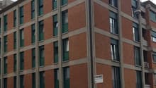 Multi-story residential building, brick walls, green shutters, air conditioning units on facade, ground floor shops, white walls