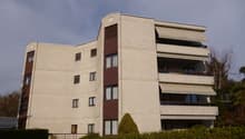 4-story apartment building with beige exterior, balconies, and a car parked in front