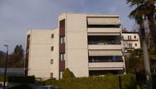 Large multi-story residential building with balconies, beige and brown color scheme