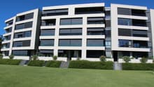 Multi-story apartment building, white exterior with glass balconies, greenery, modern design, large grassy lawn