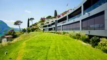 modern apartment complex on hillside, large green lawn, fenced area, glass balconies