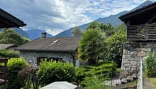 stone house with brown roof, stone walled exterior, solar panel on roof, surrounded by greenery, mountains in the background