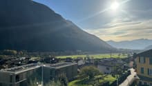 House exterior, large windows, flat roof, modern architecture, solar panels, surrounded by green grass, view of a valley, mountains in the background