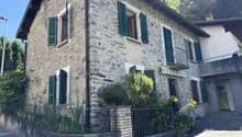 2-story stone house with green shutters, balcony, and landscaped garden in front