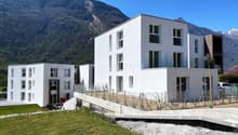 Modern white building, 4 stories, glass windows, metal railings, surrounded by mountains and greenery