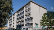 Modern apartment building, grey walls, multiple balconies, ground floor commercial space