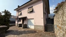 Two story house, pink exterior, white door, garage, stone walls, stairs, windows with awnings, outdoor patio