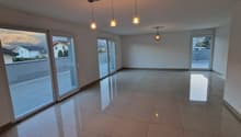 Spacious open-plan living area with large windows, hardwood floors, and modern pendant lighting fixtures. The room has a clean, minimalist design with a neutral color palette.