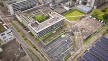 Industrial complex with multiple buildings, parking lot, solar panels, greenery, rooftop garden, wide roads, street lights