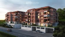 Multi-story apartment building with red brick exterior, balconies, and parking spaces in the front.