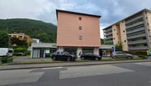 Three-story building with multiple windows, a ground-floor shop, and parking in front.