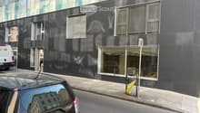 Modern building with glass facade, multiple windows, black exterior, glass door, trash bin, parked car
