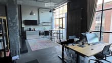 large open space, high ceilings, multiple large windows, office desk, office chairs, rug, metal shelves