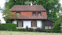 2 story house, brown roof, white walls, large chimney, multiple windows, surrounded by greenery and grass