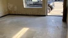 Empty room with tiled floor, wall damage, glass door and window, view of street and car.