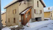 Two story house with wooden front door, brick wall, wooden window shutters, snow covered roof and yard
