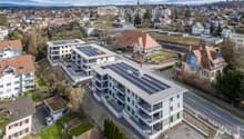 Multiple residential buildings, solar panels on rooftops, parking lot, street with traffic