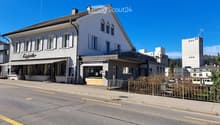 Facade with balcony, white paint, multiple windows, signage above storefront, sidewalk, and road