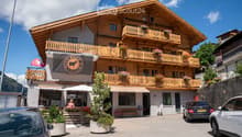 wooden exterior, multiple balconies, flag, parked cars, plants, awnings