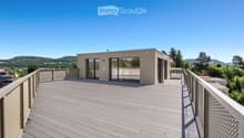 Modern rooftop terrace with wooden decking, metal railings, and panoramic views of a green landscape and hills.