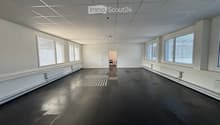 Empty room with white walls, black floor, large windows with blinds, and a doorway leading to another room.