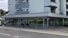 4 story building, gray exterior, glass windows, balcony, glass doors, plants, cars parked